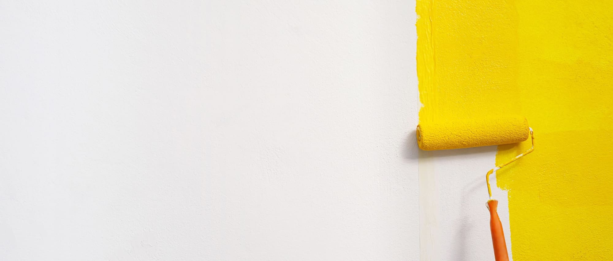 Paint roller applying bright yellow paint to a white wall